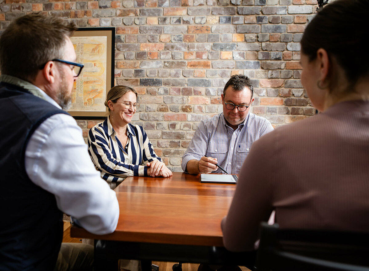 CACo. team members Erica and Peter are in a meeting with two clients. They are all sitting around a wooden table.